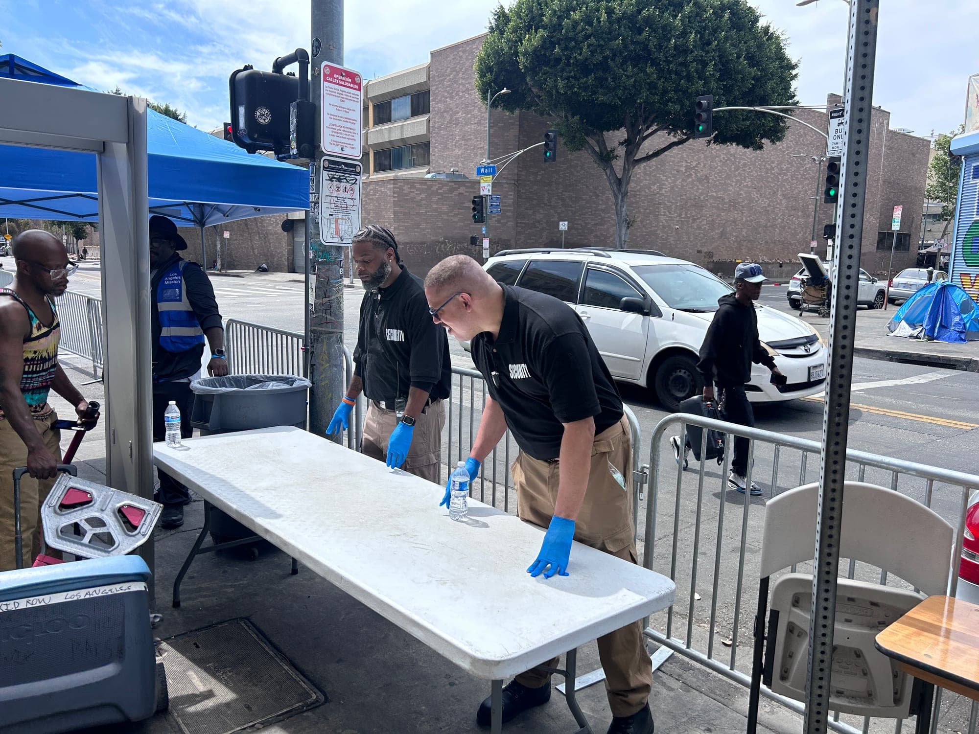 PSLA Worldwide officers in gloves staffing the entry point at the Los Angeles Mission, setting out bottled water beside the screening canopy